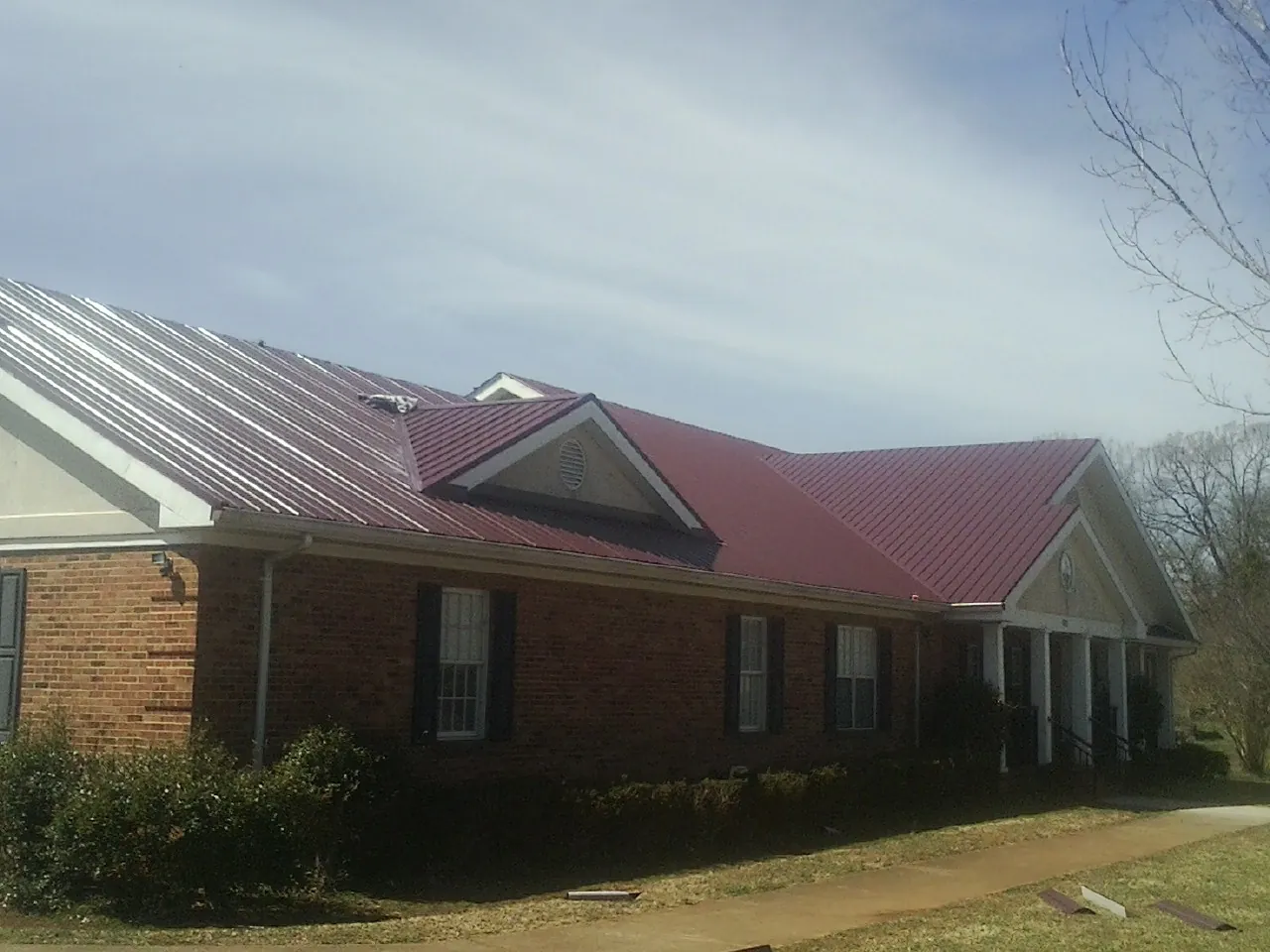 Red metal roof with gabled entries on a long brick building, from a Hail Damage Roof Repair job in Huntersville