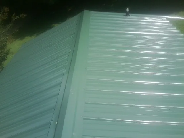 New green metal panels meeting at the ridge of a roof — Flat Roof Repair work by our crew in Huntersville