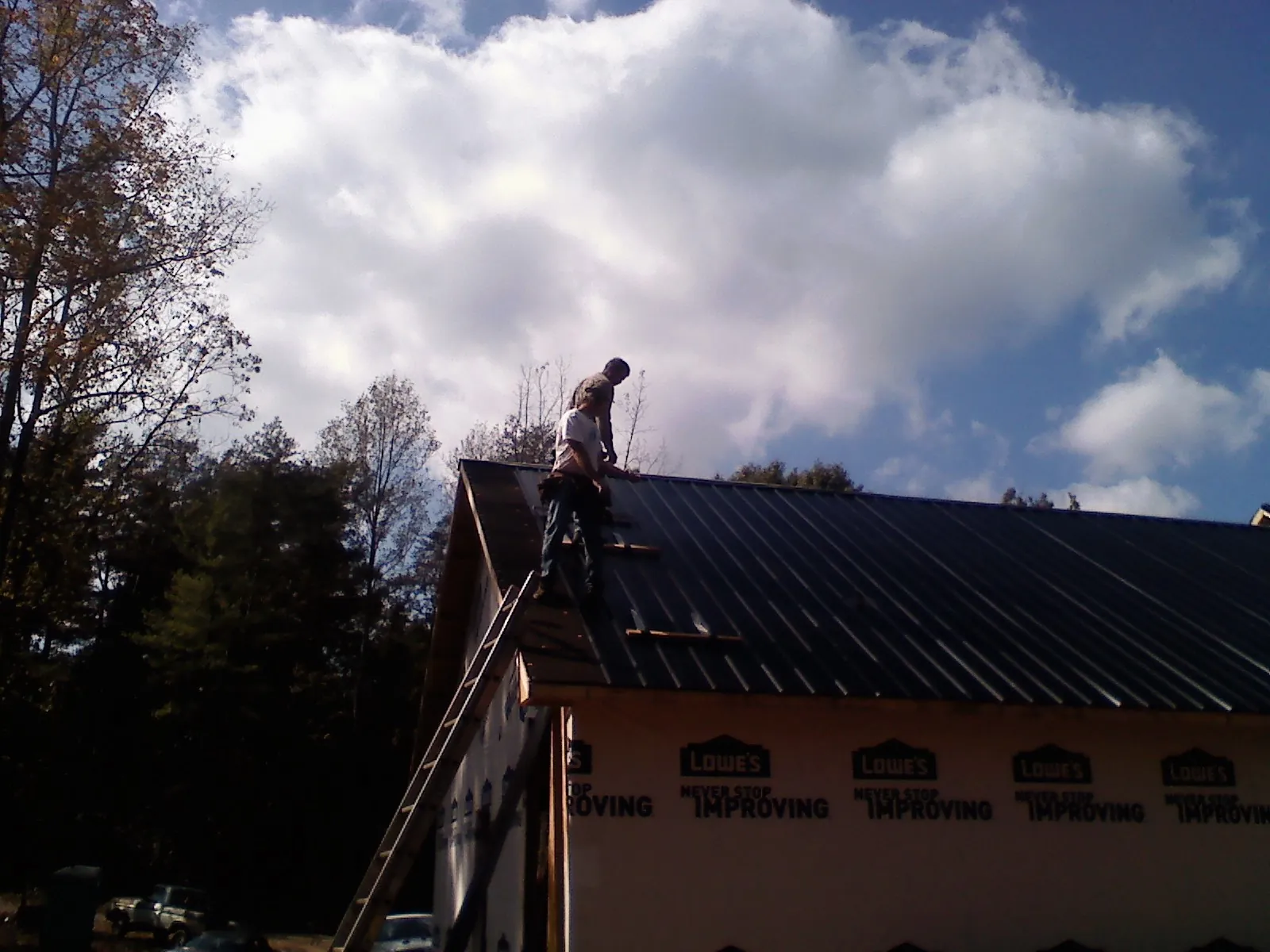 Roofer fastening dark metal panels high against a cloudy sky, from a Roof Inspection job in Huntersville