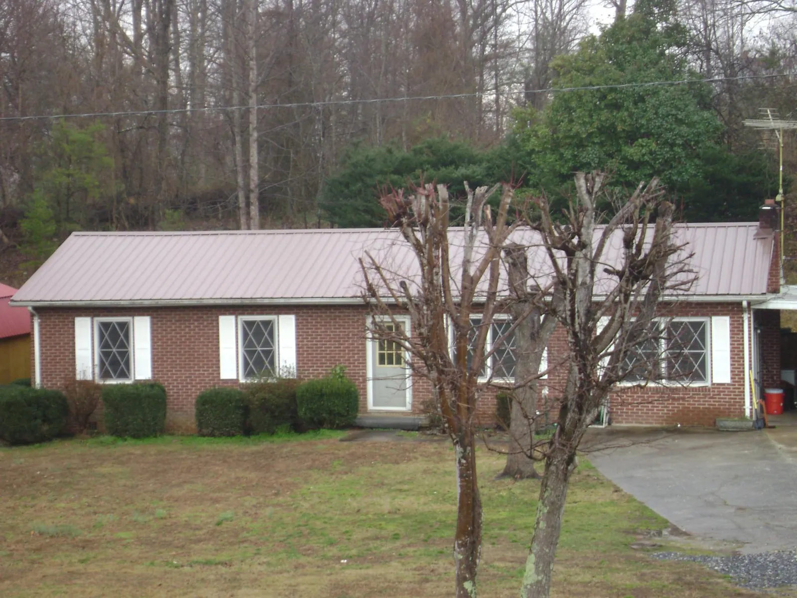 Mauve metal roof on a brick ranch home behind bare trees in Huntersville