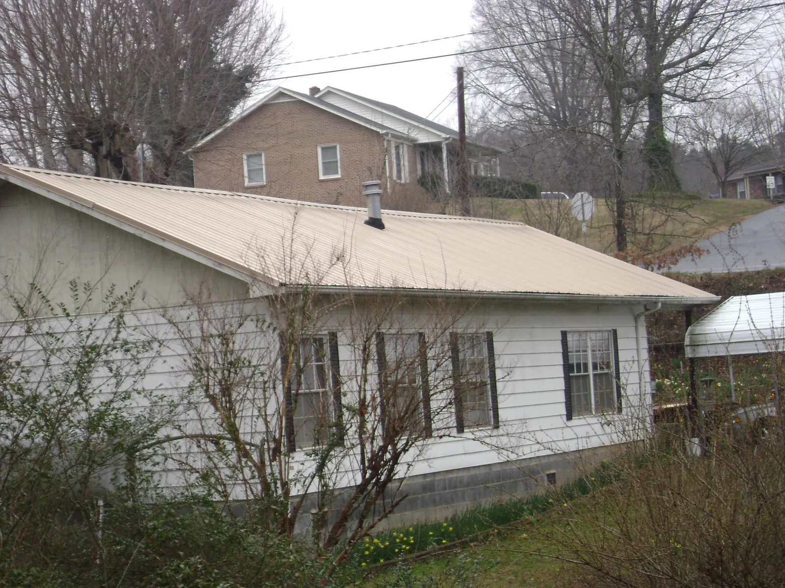 Tan metal roof on a white sided house set into a hillside — Commercial Roofing by Roofing Brothers in Huntersville