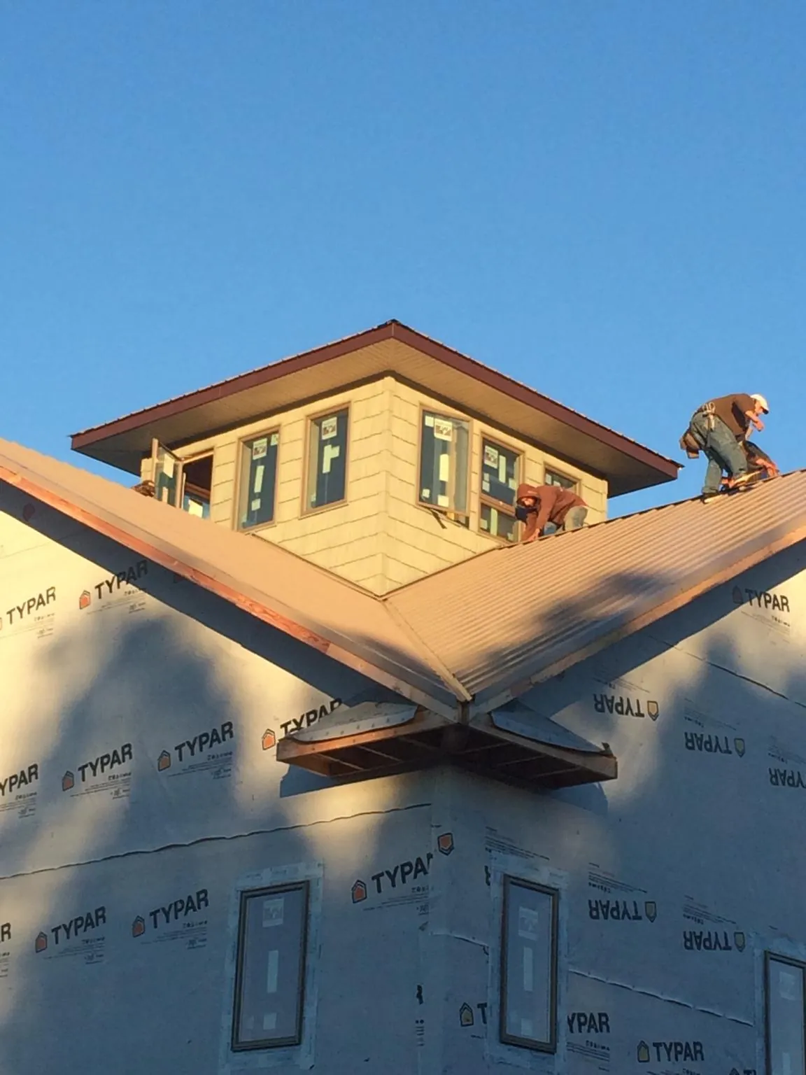 Roofers working around a rooftop cupola on a new metal roof at sunset — Roof Waterproofing in Huntersville by Roofing Brothers